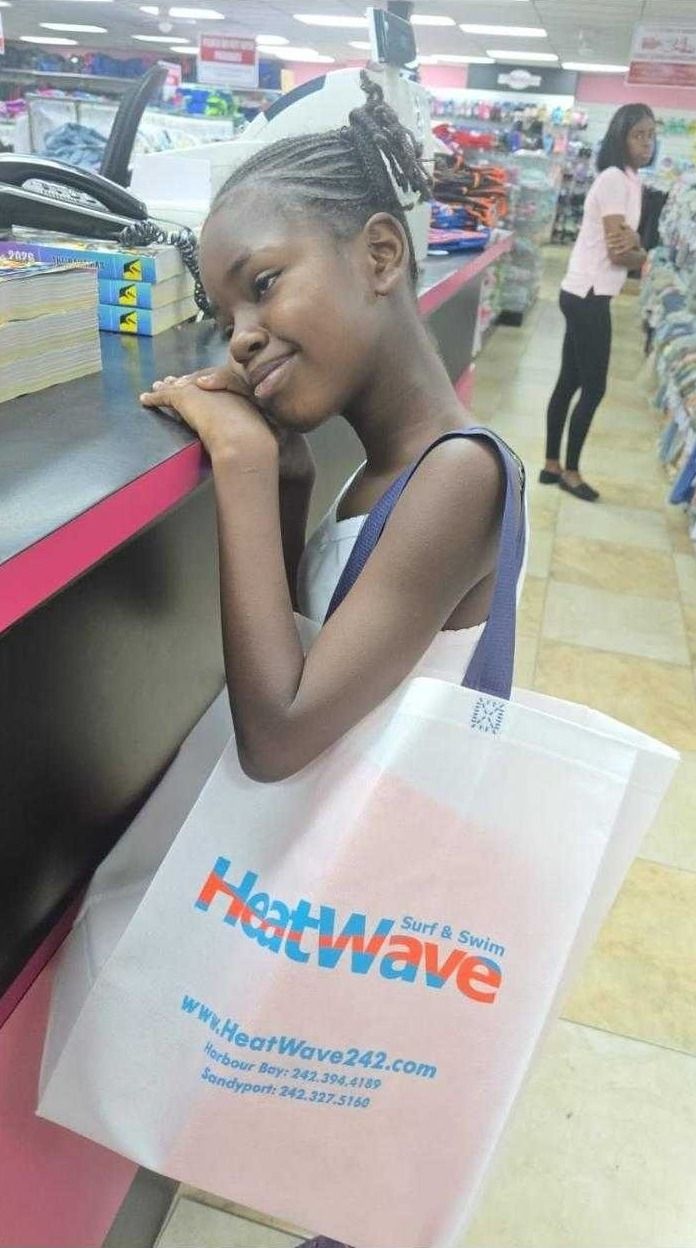 A smiling girl leans on a store counter with a Heat Wave tote bag during back-to-school shopping