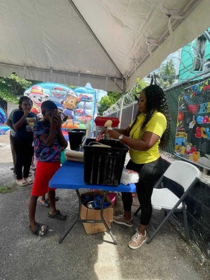 A woman in a yellow UAC polo hands out treats from a table to children under a tent