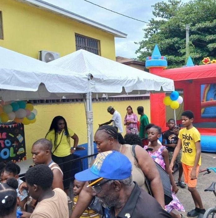Families and children crowd under white tents beside a bounce house at the Back to School event