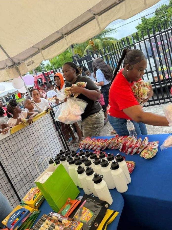 Two women hand out bags of popcorn and treats at a table of water bottles and school supplies
