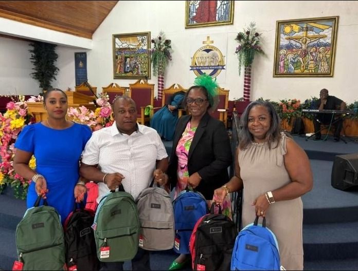 Three women and a man hold new backpacks in green, gray, blue, red and black inside a church