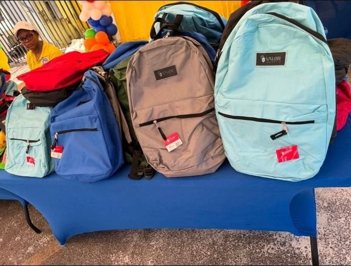 Light blue, blue, gray and red backpacks are stacked on a blue table at the giveaway