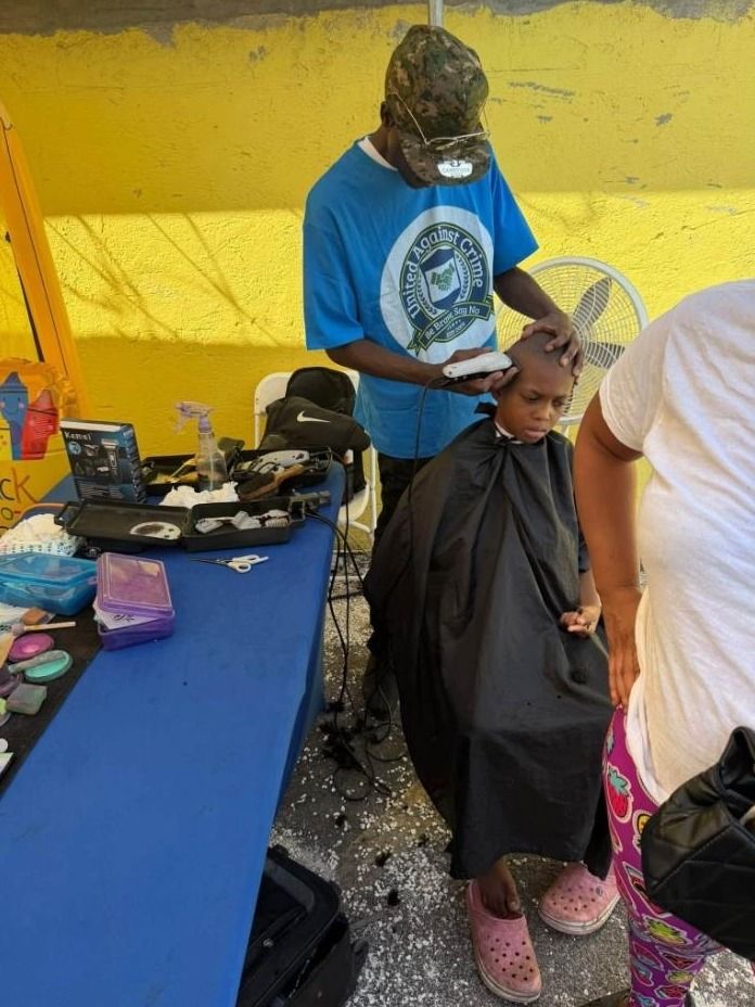 A man in a United Against Crime shirt gives a child a haircut at an outdoor barber station