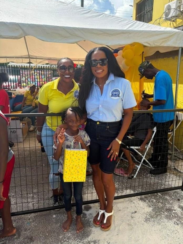 Two women in yellow and light blue polos pose with a girl holding a yellow polka dot gift bag