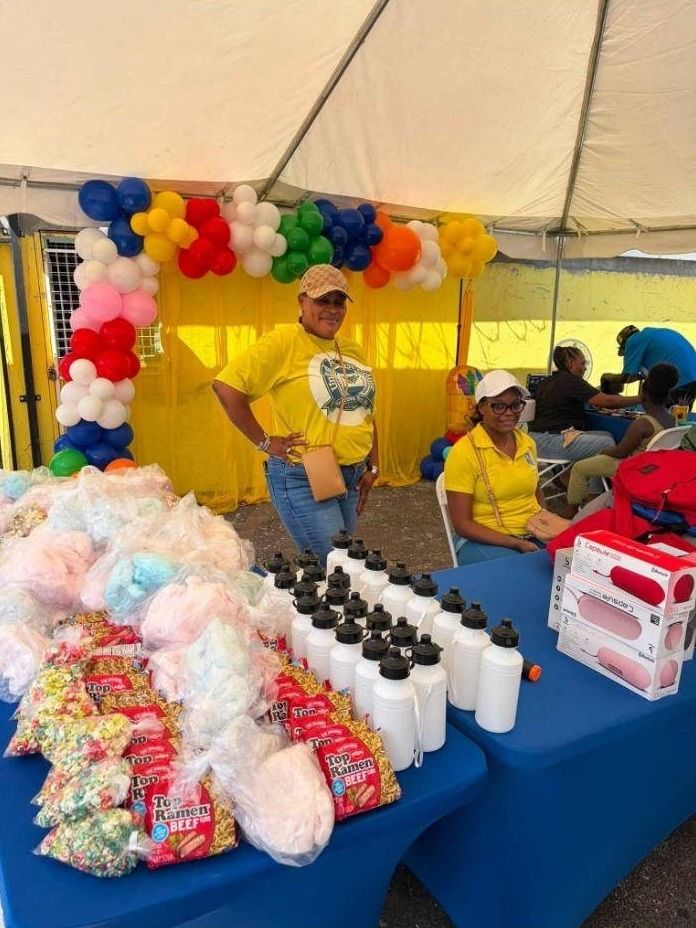 Volunteers in yellow shirts behind tables of cotton candy, snacks and water bottles under a balloon arch