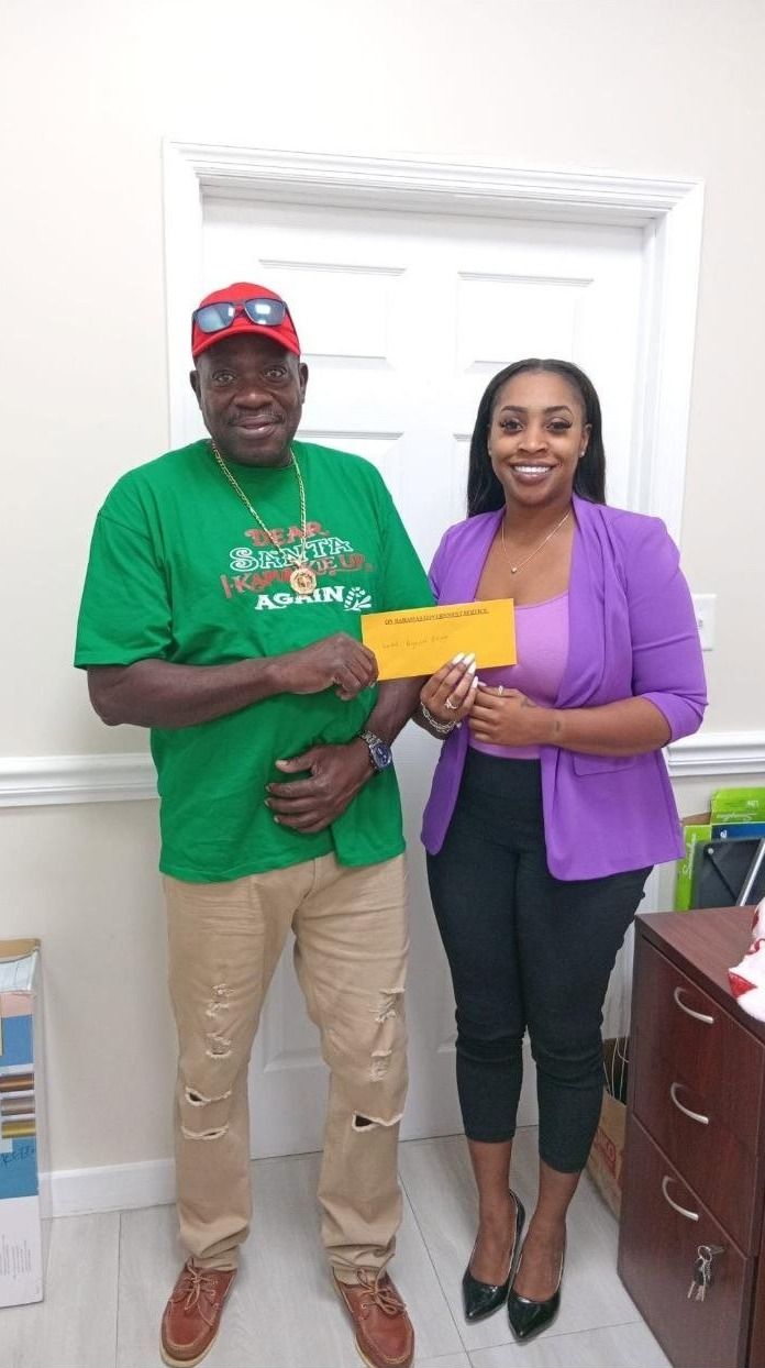 A man in a green Christmas shirt and a woman in a purple blazer hold an envelope in an office