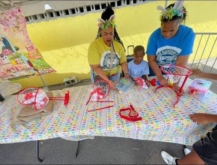 Two women in bunny-ear headbands and a small boy sit at a ring toss game table