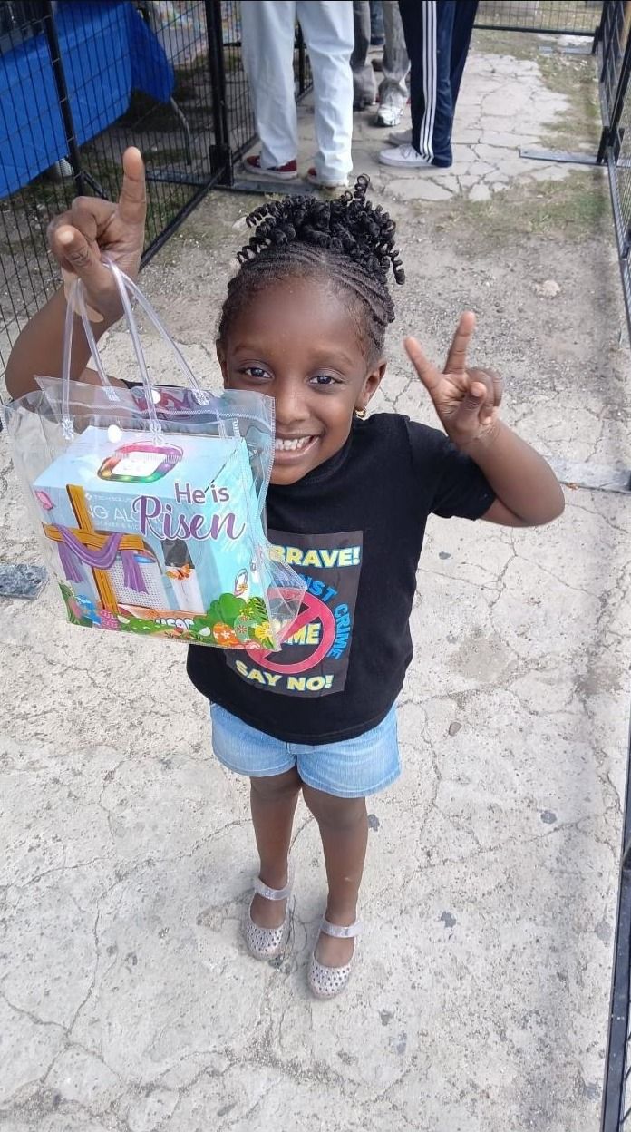 A smiling girl in a Be Brave Say No shirt holds up a He Is Risen gift bag
