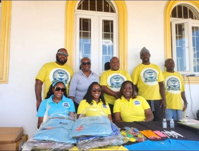 Volunteers in yellow United Against Crime shirts pose behind a table of school supplies and wrapped backpacks