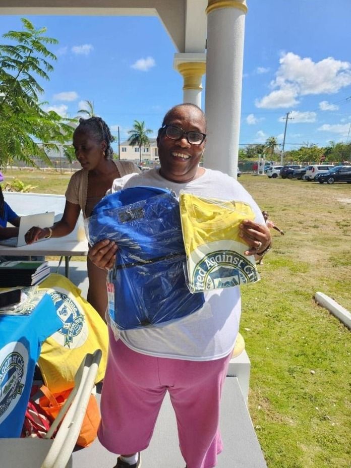 A smiling woman holds a wrapped blue backpack and a wrapped yellow United Against Crime shirt on a porch