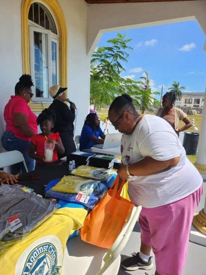 Volunteers sort backpacks and shirts at a table on a covered porch while a woman sings into a microphone