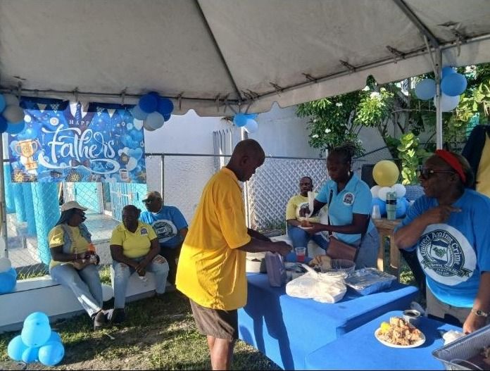 A man in a yellow shirt stands at a food table while volunteers in United Against Crime shirts serve