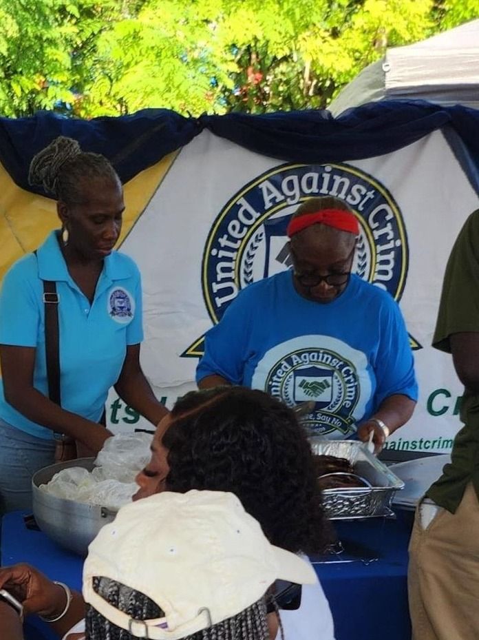 A woman in a light blue polo and a woman in blue serve food in front of the banner
