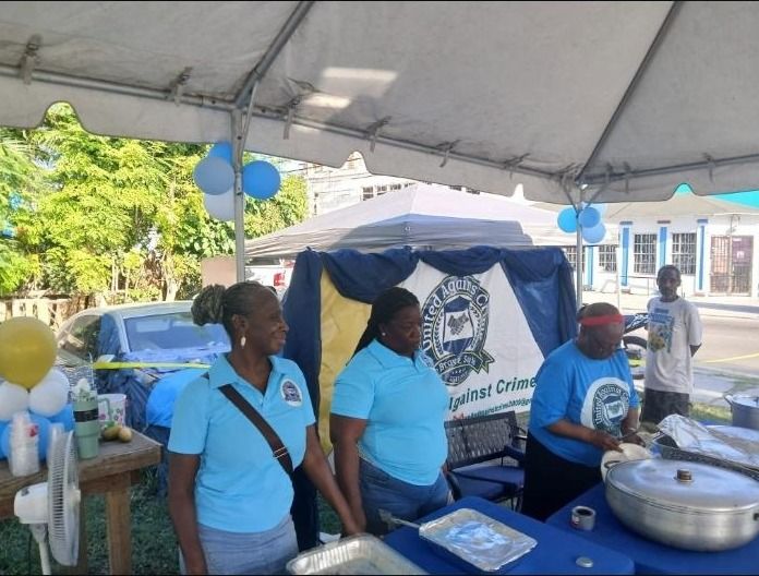 Two women in light blue polos and one in blue serve food at the banner table