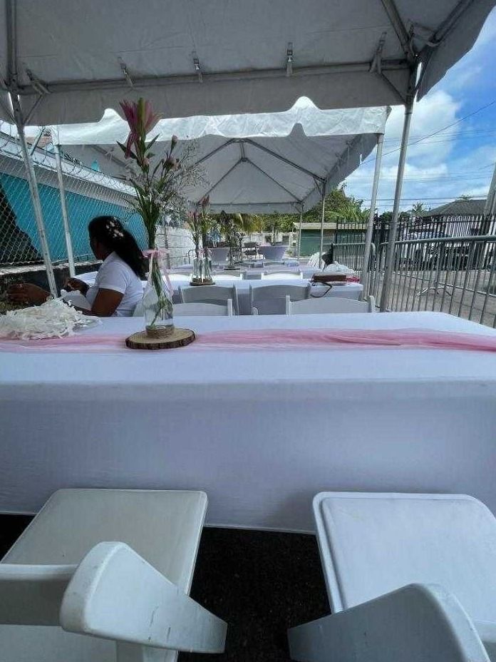 A long white table with a pink runner and flower vases sits under a tent before guests arrive