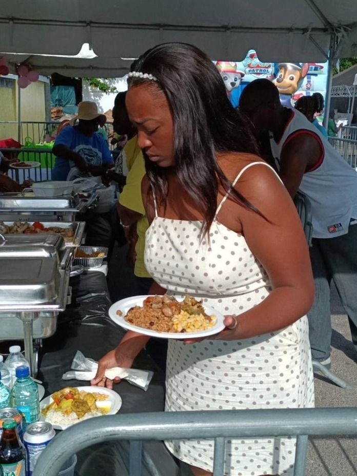 A woman in a polka dot dress carries a plate of rice, corn and stew along the buffet