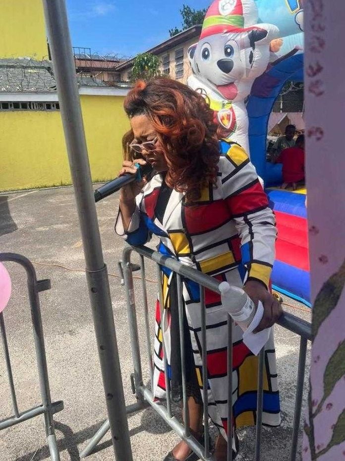 A woman in a colorful patterned coat speaks into a microphone beside a bounce house