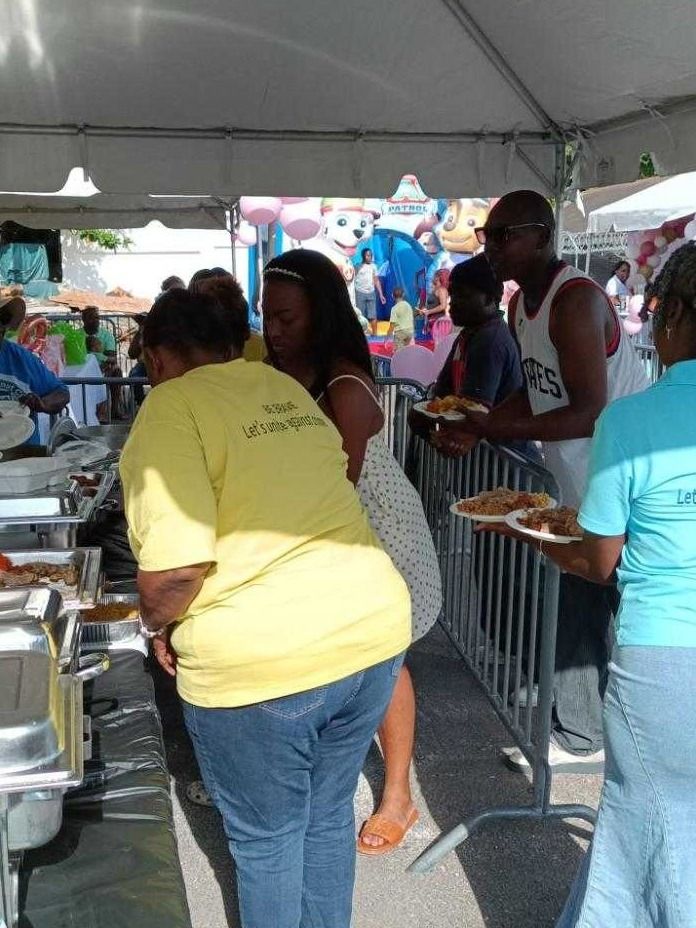Guests holding plates line up at the buffet beside a Paw Patrol bounce house while volunteers serve