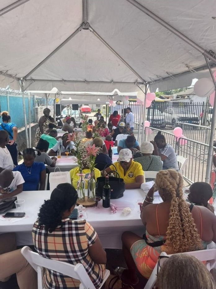 Guests sit at long tables with flower vases under a large tent at the Mother's Day celebration