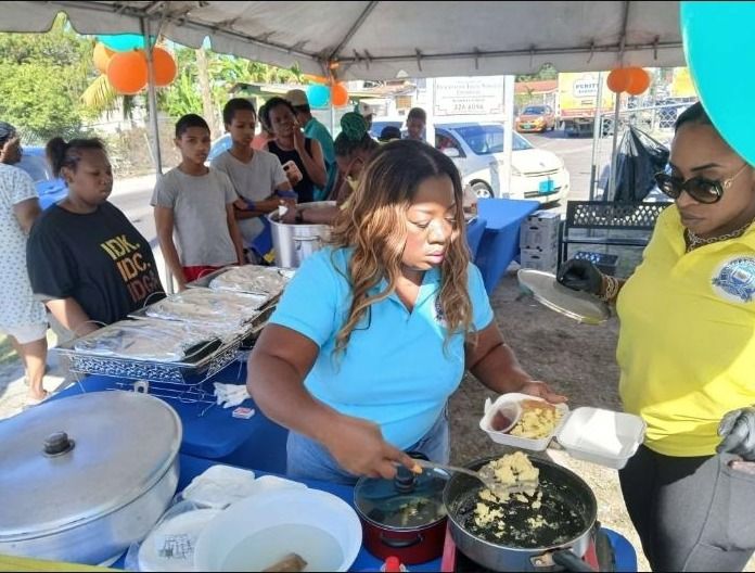 A woman in a light blue polo spoons scrambled eggs into takeout containers beside a volunteer in a yellow polo